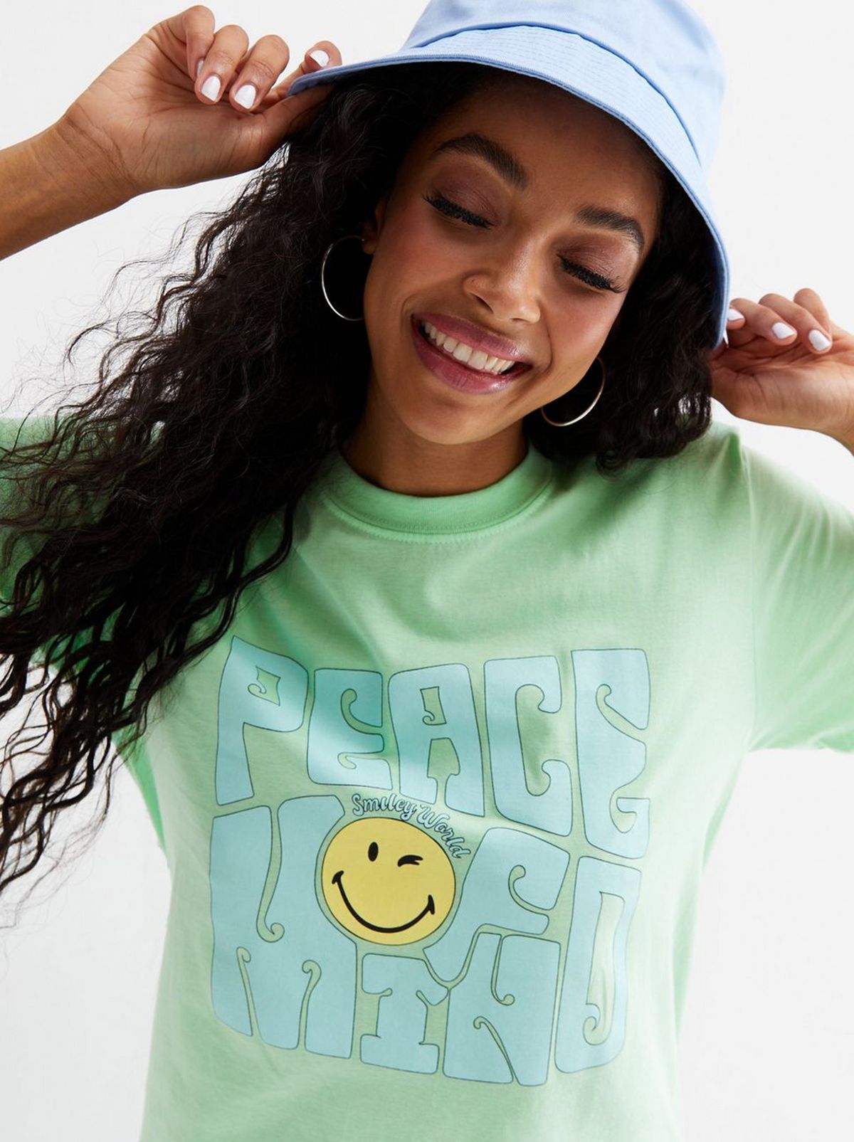 A women is wearing a light blue bucket hat and a light green printed T shirt