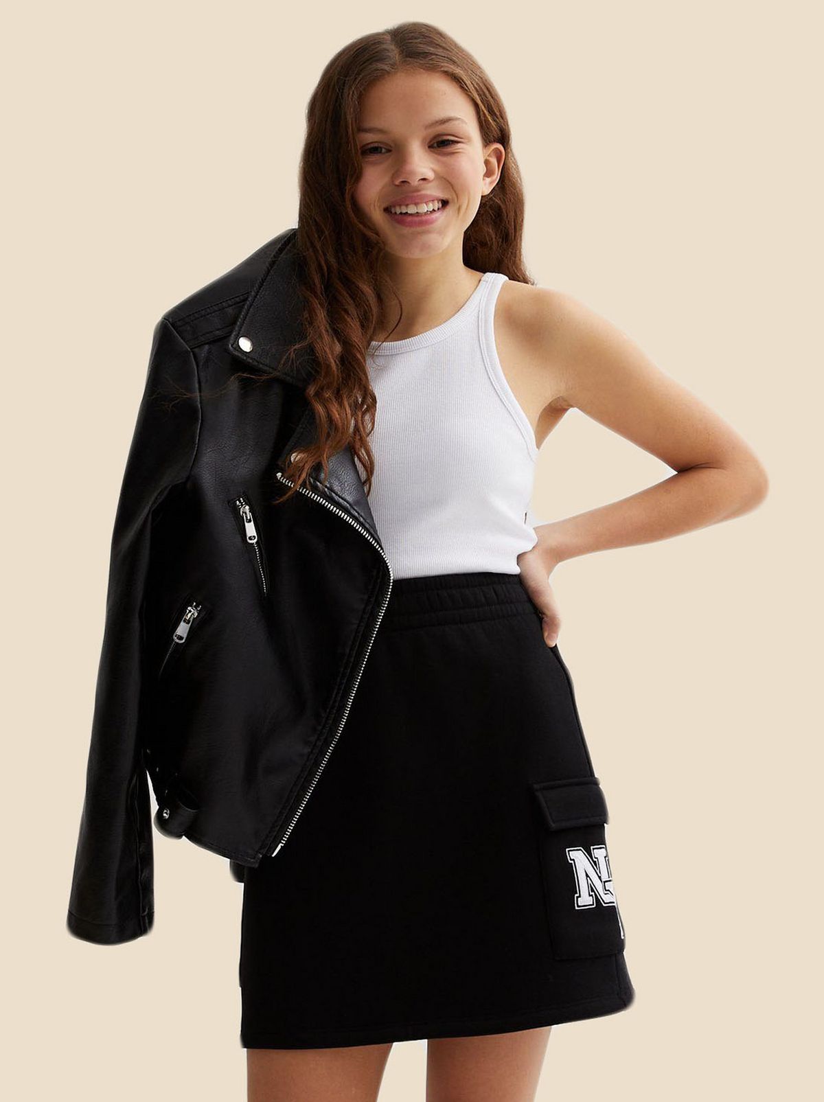 Girl wearing a white vest top, black cargo skirt and denim jacket​