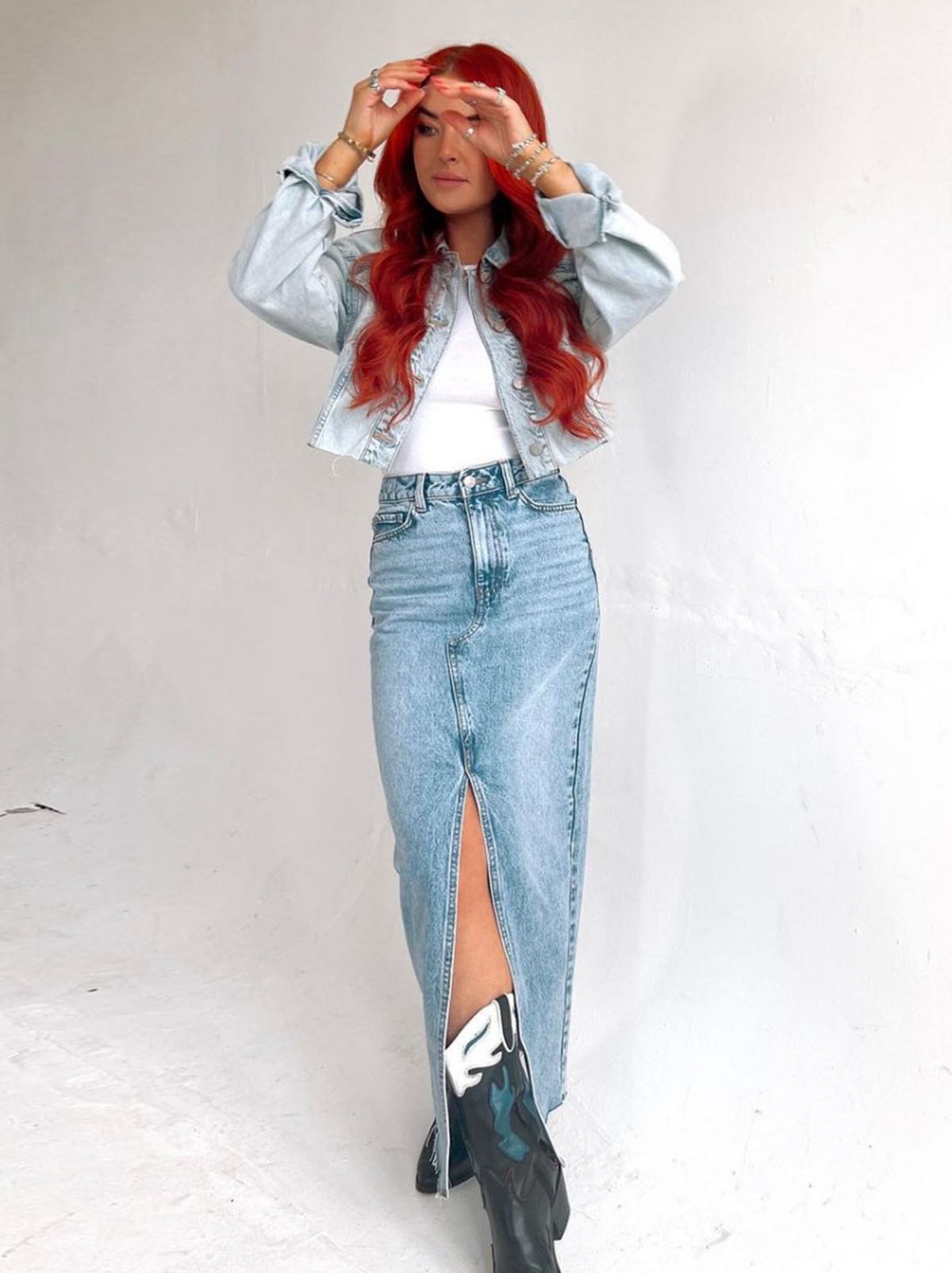 A model is standing with their ankles crossed while wearing a blue shirt, a white top and a denim midi skirt