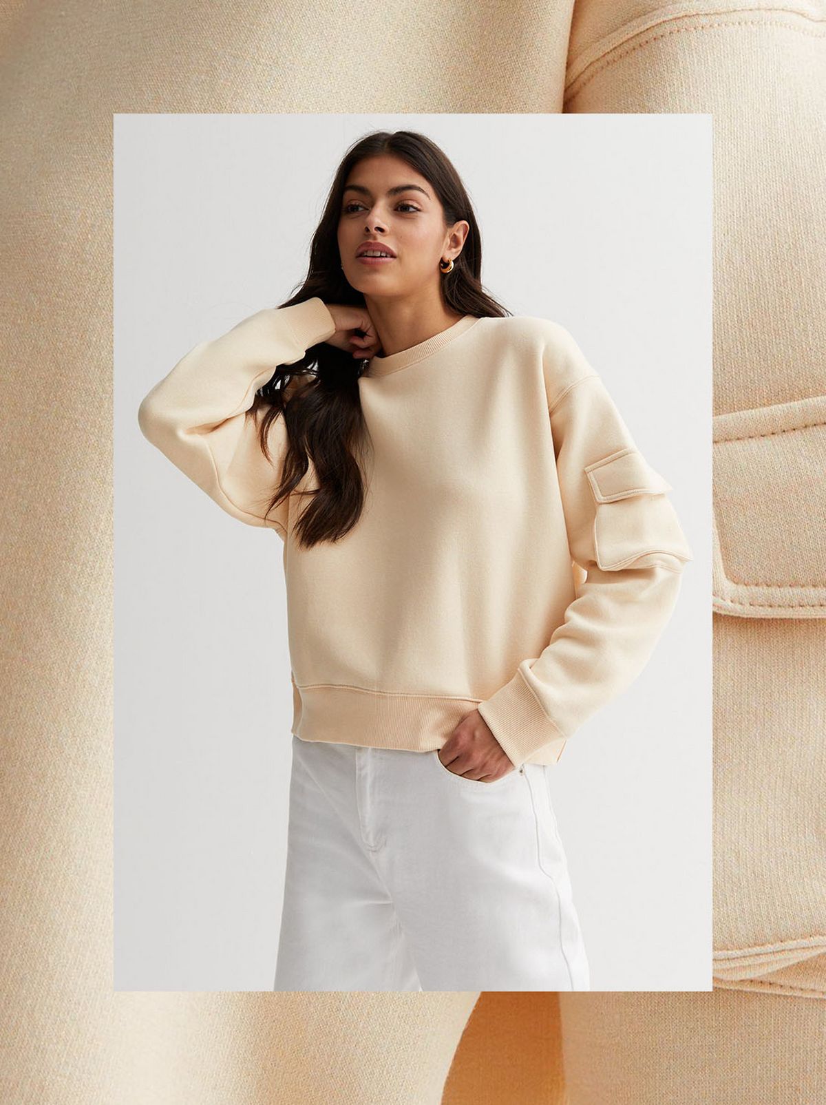 A model stands in front of a white background wearing a cream crew neck sweatshirt with a utility pocket on the arm	