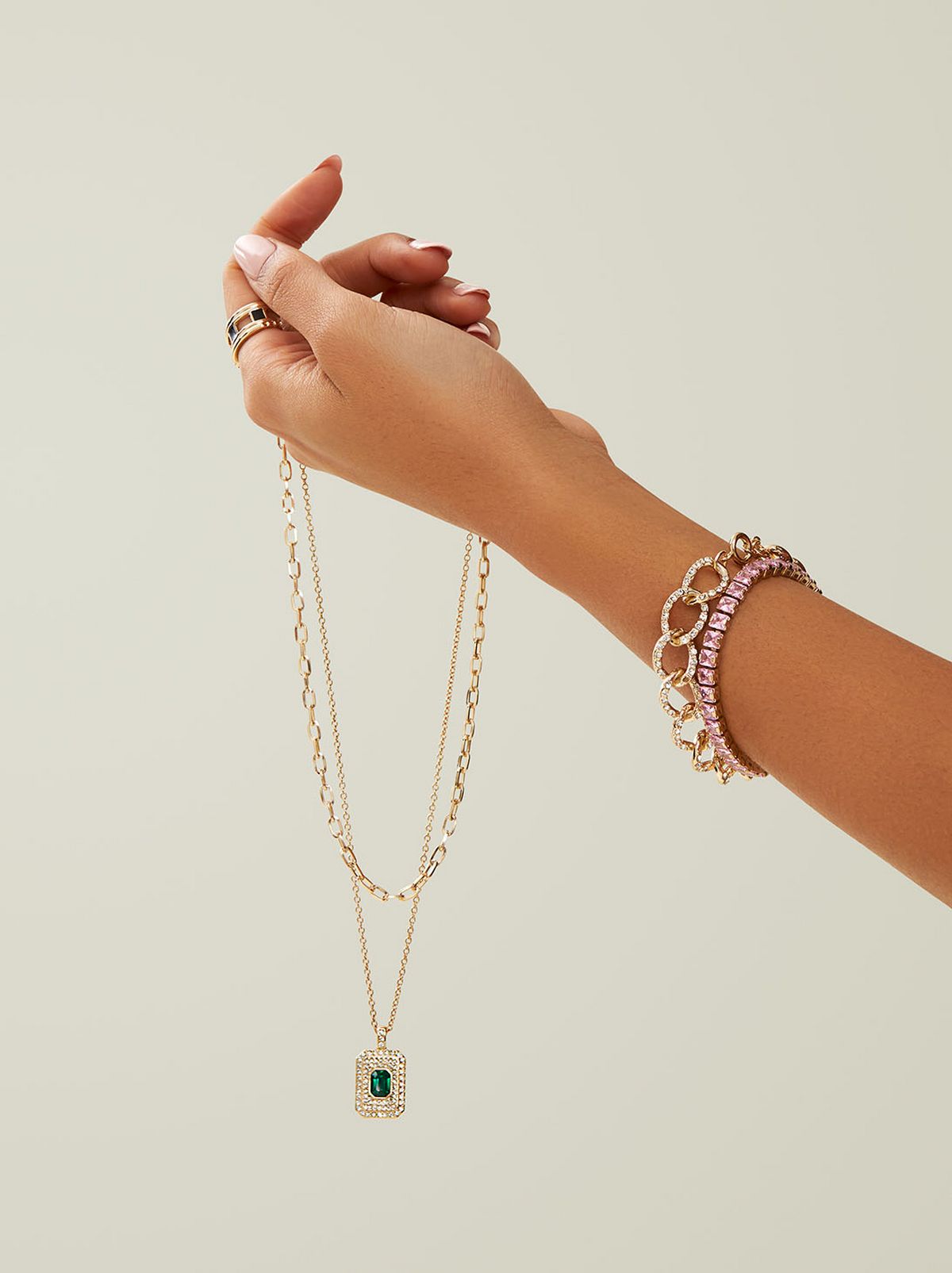 A person holds a pendant necklace with a bracelet on their wrist	