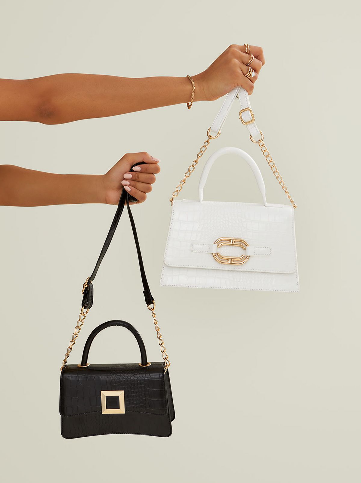 Two hands are held outstretched in front of a blank background holding a white and a black handbag in each hand	