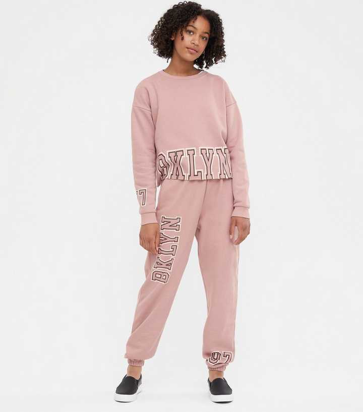 https://media2.newlookassets.com/i/newlook/693970517/girls/girls-clothing/girls-trousers/girls-pale-pink-bklyn-logo-joggers-set.jpg?strip=true&qlt=50&w=720
