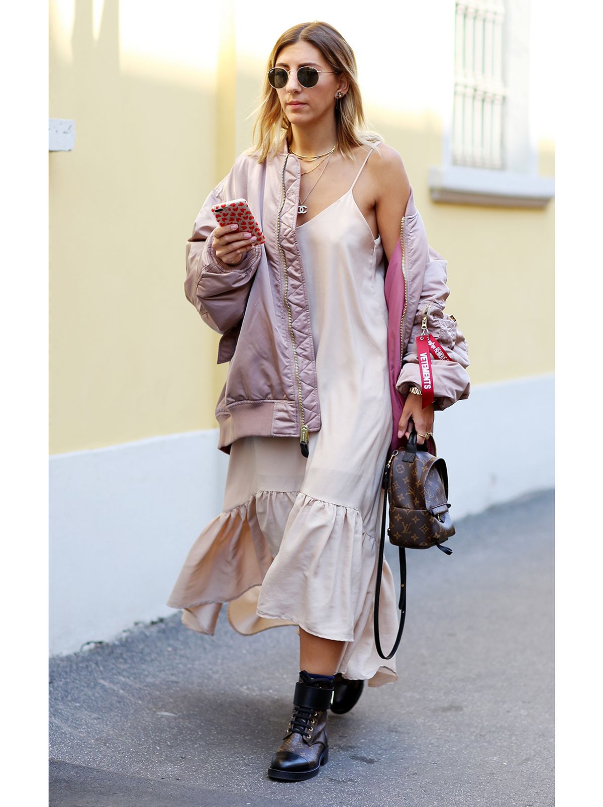 Woman wearing a frill hem slip dress with a bomber jacket, black chunky boots and sunglasses