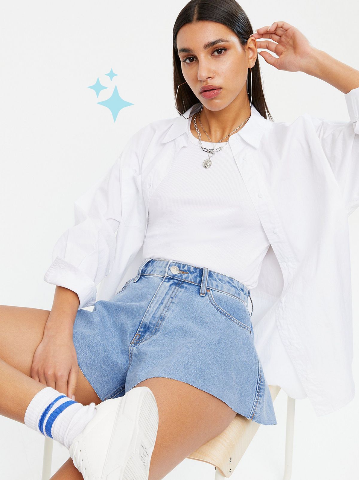 Woman wearing a Blue Denim Cut Off Shorts, white oversized shirt and trainers